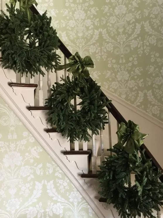 a trio of evergreen wreaths with emerald ribbon bows for decorating your banister for Christmas