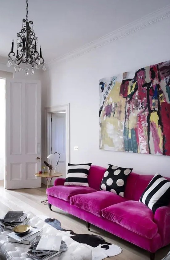 a catchy living room with a magenta sofa and printed pillows, a bold artwork, a cowhide rug and a glass coffee table plus a crystal chandelier