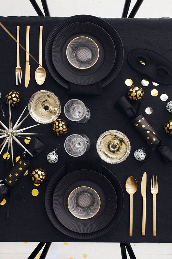 a modern black and gold NYE party tablescape with black plates, gold and black ornaments, a large star and disco balls