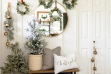 19 lovely Christmas wall decor with greenery and pinecone wreaths hanging down, with evergreens and bells plus a potted Christmas tree