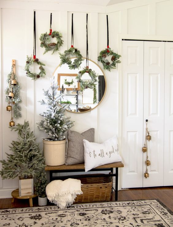 lovely Christmas wall decor with greenery and pinecone wreaths hanging down, with evergreens and bells plus a potted Christmas tree
