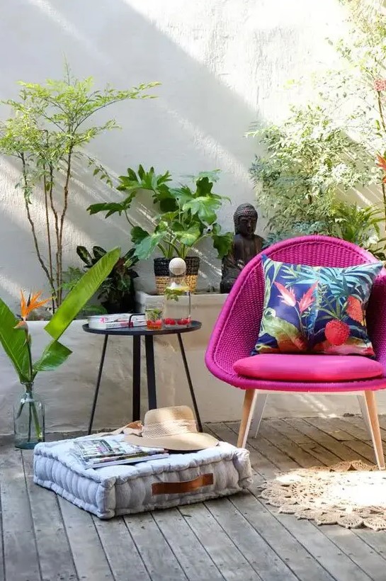 a cool outdoor nook with a woven magenta chair, a side table, a cushion, potted plants and beautiful Asian inspired decor