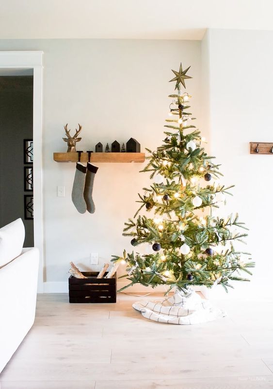 a minimalist Christmas tree decorated with black and white ornaments and lights and with its base covered with fabric