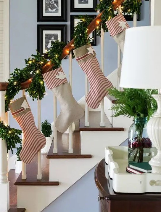 an evergreen and lights Christmas garland that wraps the banister and striped stockings are great decor for a banister