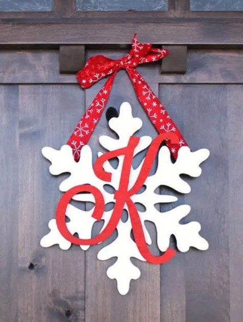 a snowflake door hanger with a monogram and red ribbon is a classic Christmas decor idea suitable for many outdoor spaces