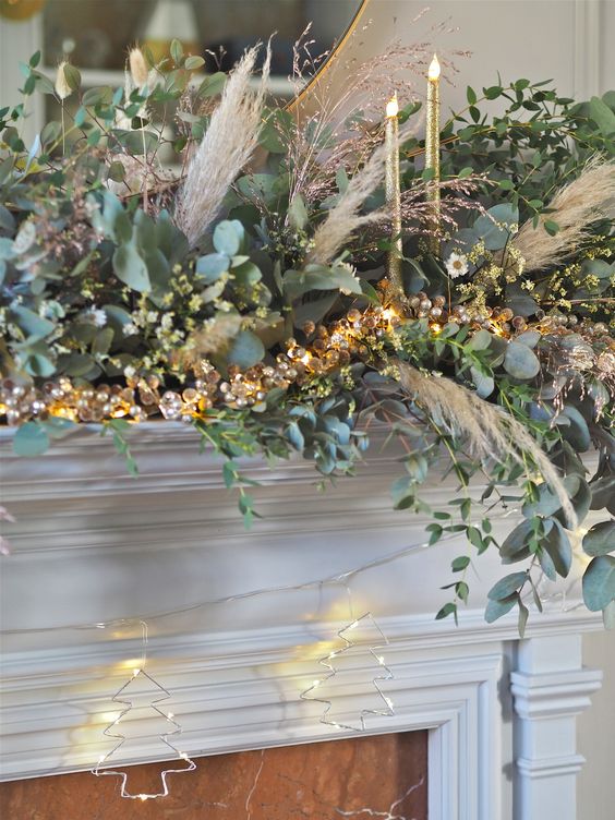 a super lush Christmas mantel garland of greenery, lights and pampas grass plus tall and thin candles is amazing