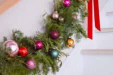 21 an evergreen Christmas garland dotted with super colorful ornaments and red ribbon bows is a fantastic idea for a banister