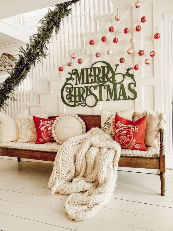 a Christmas entryway with red, green and white ornaments hanging over the space, green letters and a bench styled with red and white pillows