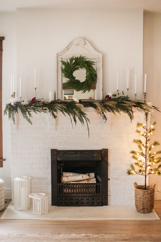 a boho Christmas mantel decorated with greenery, pampas grass and bold blooms, tall and thin candles and an evergreen wreath on the mirror