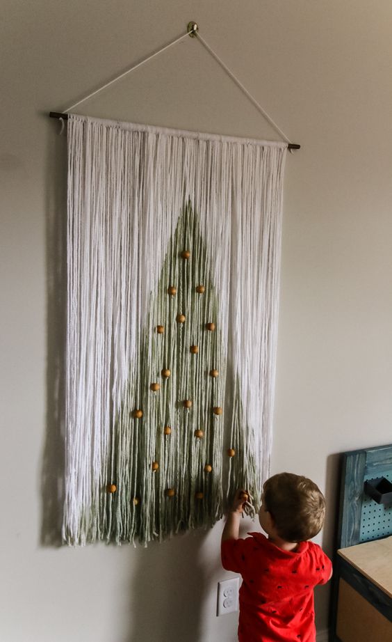 a Christmas wall hanging of long fringe showing off a Christmas tree with wooden beads as ornaments is a lovely decoration