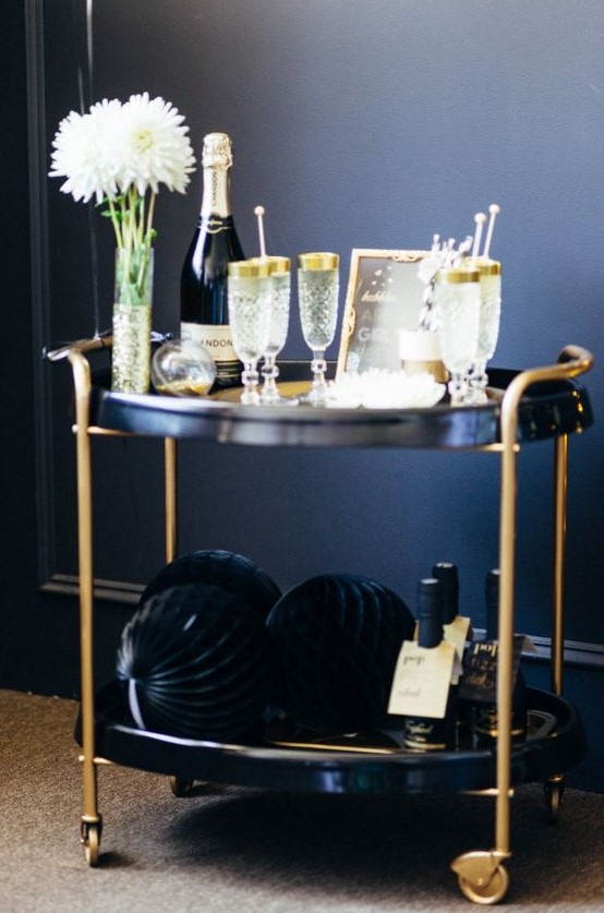 a black and gold cart with gold rim glasses and large pipe balls for an elegant feel at your NYE party