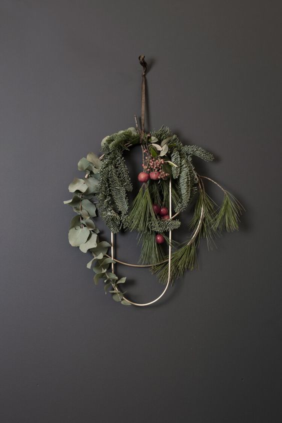 a modern Christmas wreath of a gold circle and curve, with evergreens, greenery and berries is a lovely idea