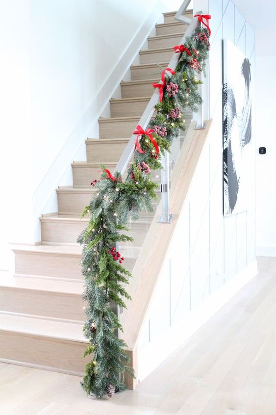 an evergreen Christmas garland with lights, berries and red bows plus pinecones looks very festive and super natural