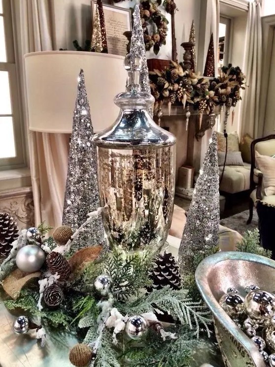 a silver Christmas centerpiece of evergreens, pinecones, silver ornaments, silver sequin cone trees and a mercury glass jar
