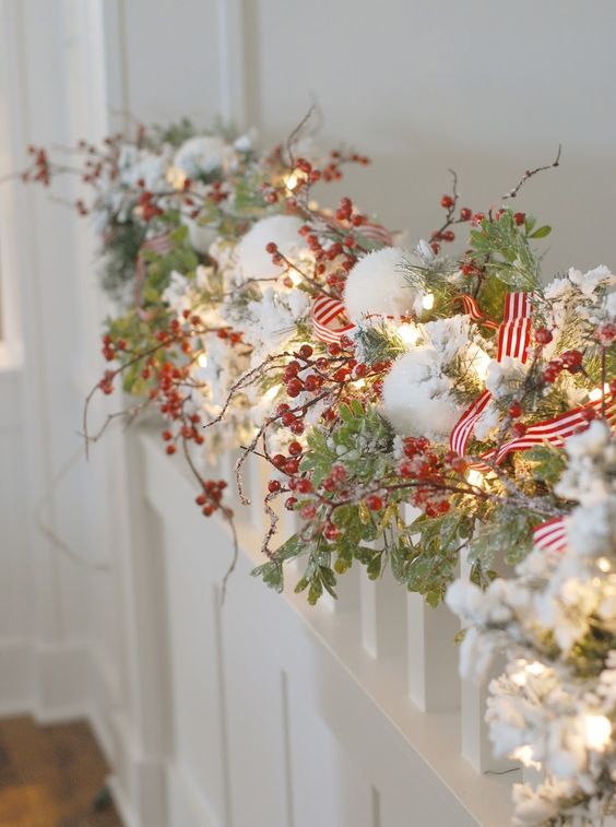 an evergreen Christmas garland with snow, red berries, striped ribbons and lights is a cool idea for winter