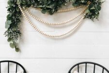 28 a lovely Christmas wall decoration of greenery, wooden bead garlands is a cool solution for any space of your home