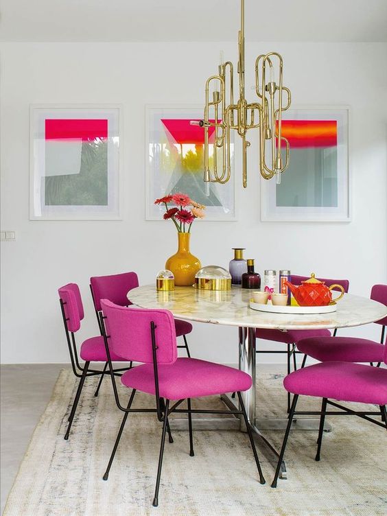 a sophisticated living room wiht a gallery wall, a round table, magenta chairs, a beautiful gold chandelier over the table