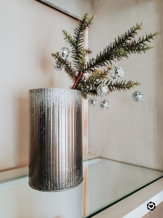 a tin vase with evergreens adn tiny disco balls as decor is a lovely idea for Christmas and NYE parties