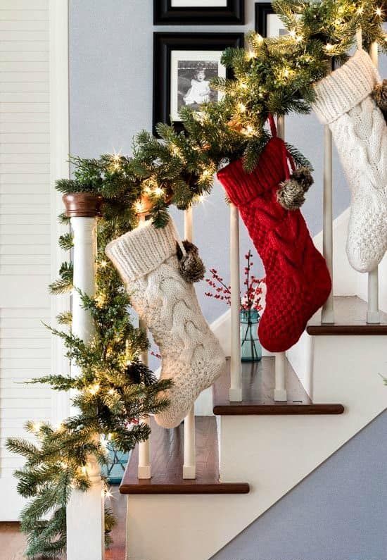 an evergreen garland with lights and pinecones plus red and white stockings hanging down are a great Christmas decoration for a banister
