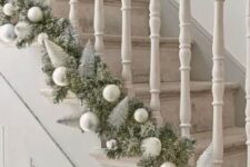 34 an evergreen garland with silver and matte silver ornaments and bottle brush Christmas trees is a chic idea for styling a staircase