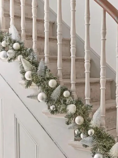 an evergreen garland with silver and matte silver ornaments and bottle brush Christmas trees is a chic idea for styling a staircase