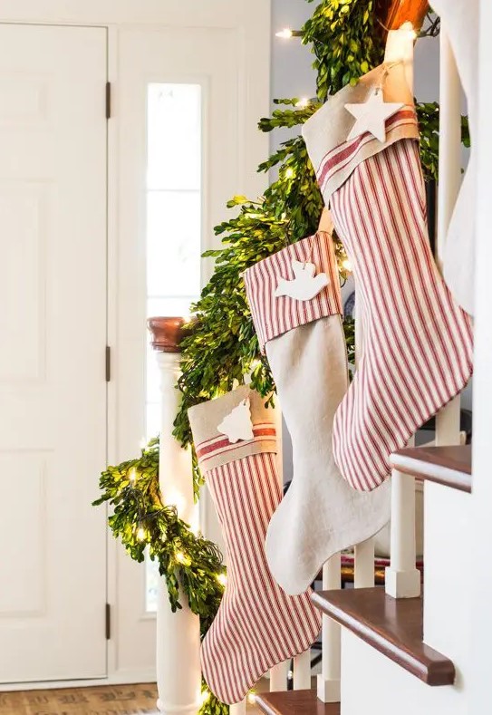 Christmas railing decor with striped stockings, clay tags, evergreens and lights is amazing, chic and cool