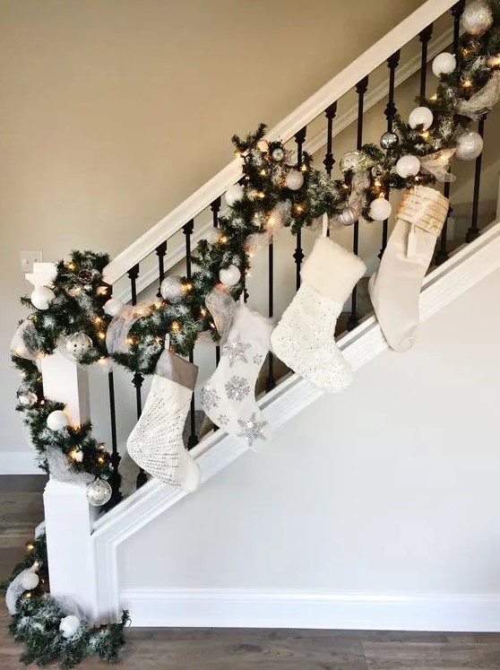 Christmas railing decor with white embellished stockings, an evergreen garland with lights and white and silver ornaments