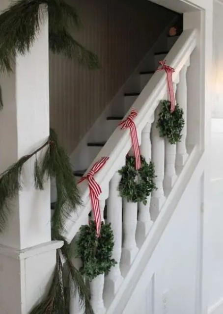 cool eucalyptus wreaths with red striped ribbon and an evergreen garland are a nice combo for Christmas staircase decor
