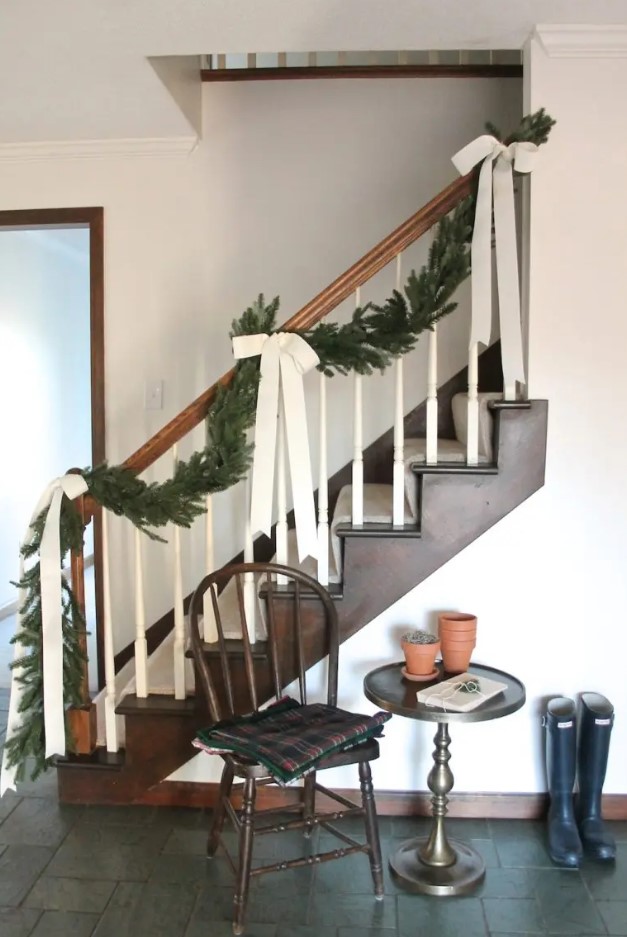 elegant farmhouse Christmas railing decorated with an evergreen garland with large neutral bows is a stylish idea