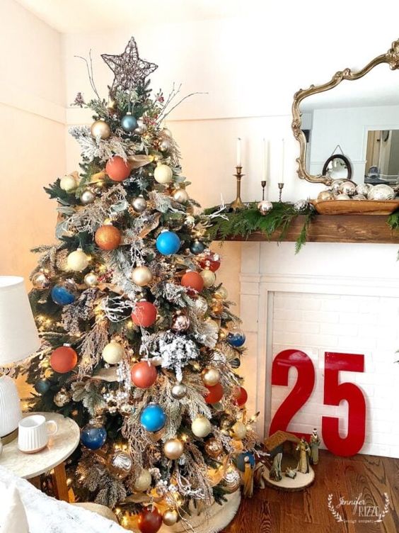 a flocked Christmas tree decorated with creamy, copper, rust, blue and gold ornaments, branches and twigs, greenery and a star topper
