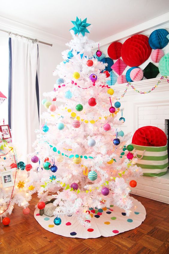 a white Christmas tree decorated with super bright ornaments and garlands, matching paper pompoms and a tree skirt