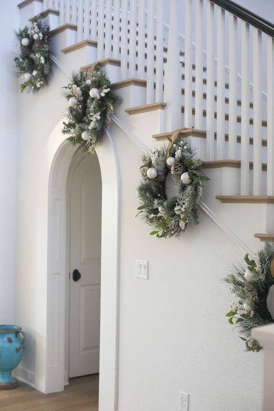 pretty evergreen wreaths with pinecones and white ornaments will beautifully decorate your Christmas banister