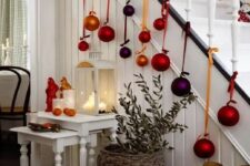 53 some candle lanterns on the stairs and large colorful Christmas ornaments hanging down from the stairs are amazing for holiday decor