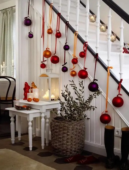 some candle lanterns on the stairs and large colorful Christmas ornaments hanging down from the stairs are amazing for holiday decor