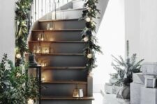 57 a Scandinavian staircase with small lanterns, greenery, lights and pinecone garlands on the railings looks beautiful