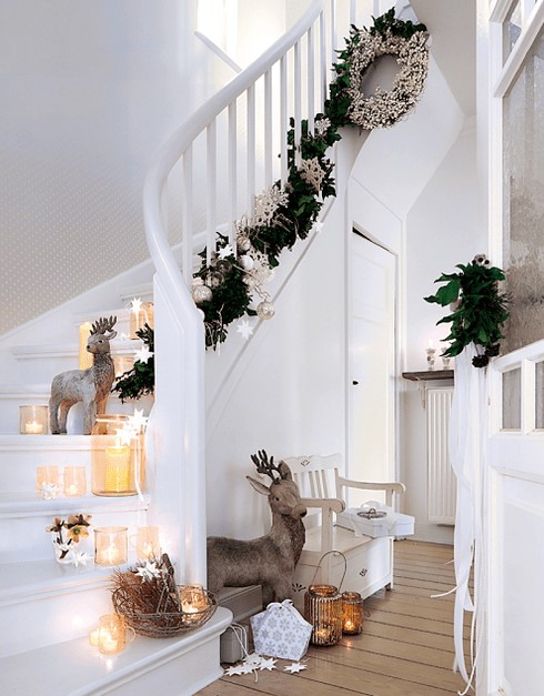 Scandinavian stairs decor with candle lanterns and candleholders, deer, stars and an evergreen garland with silver and white ornaments