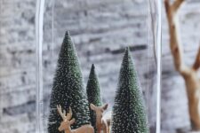 a Christmas terrarium with deer figurines, bottle brush Christmas trees and some logs is a lovely idea