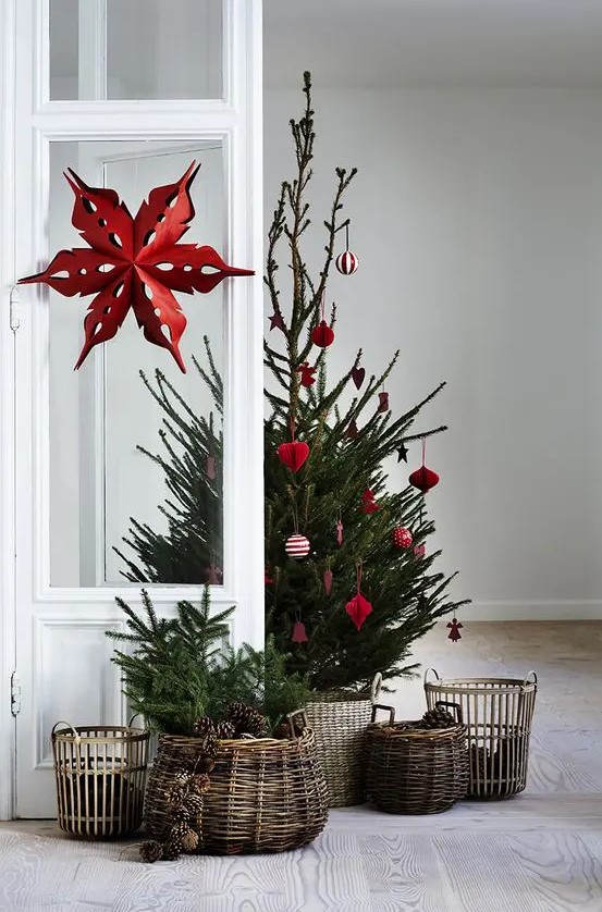 a Christmas tree in a basket with red ornaments and some baskets with evergreens and pinecones around create a cozy rustic feel