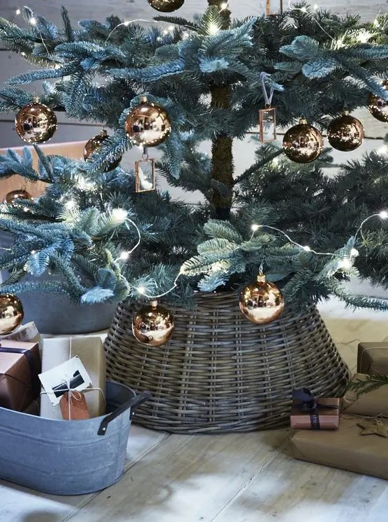 a Christmas tree with copper ornaments and a basket that hides the tree base looks very cozy and elegant at the same time, with a rustic feel