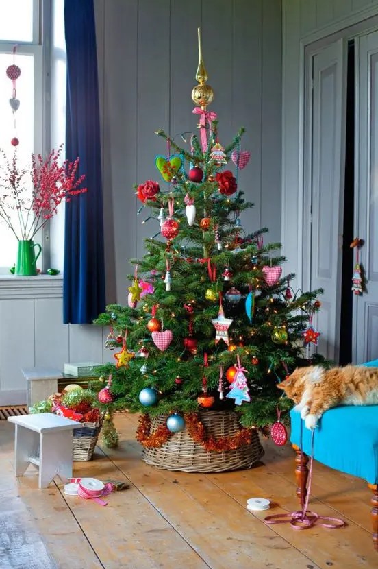 a Christmas tree with lots of bright vintage ornaments and lights in a basket looks very cool and sweet and matches vintage Christmas decor