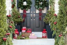 a beautiful Christmas porch with evergreens, red ornaments, foliage wreaths, gift boxes and red candle lanterns