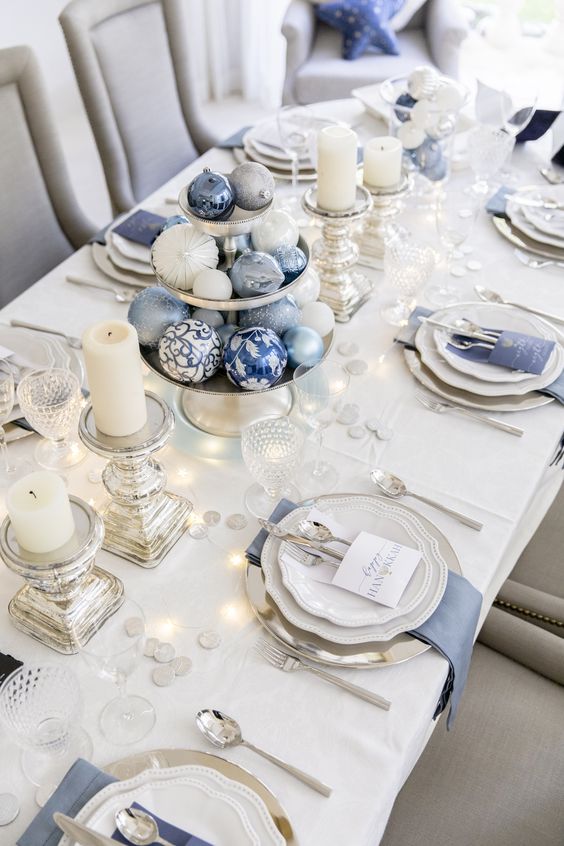 a beautiful Christmas tablescape with silver chargers and cutlery, candleholders and stands, blue and white Christmas ornaments and napkins
