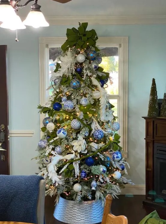 a beautiful Christmas tree with white feathers and fabric blooms, blue and white ornaments, a large green bow on top is amazing