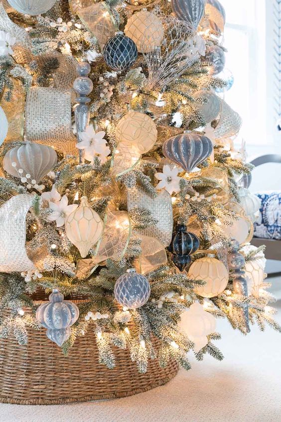 a beautiful flocked Christmas tree decorated with lights, pastel blue, white and silver ornaments, ribbons, white blooms is super chic and glam