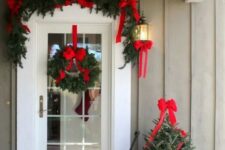 a bright and cool Christmas porch with an evergreen garland with red bows, a wreath, a mini tree with lights and gifts