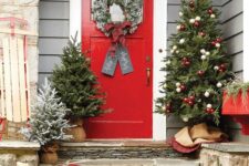 a bright festive porch with Christmas trees and red and white ornaments, firewood in a bucket, red rubber boots and an evergreen garland
