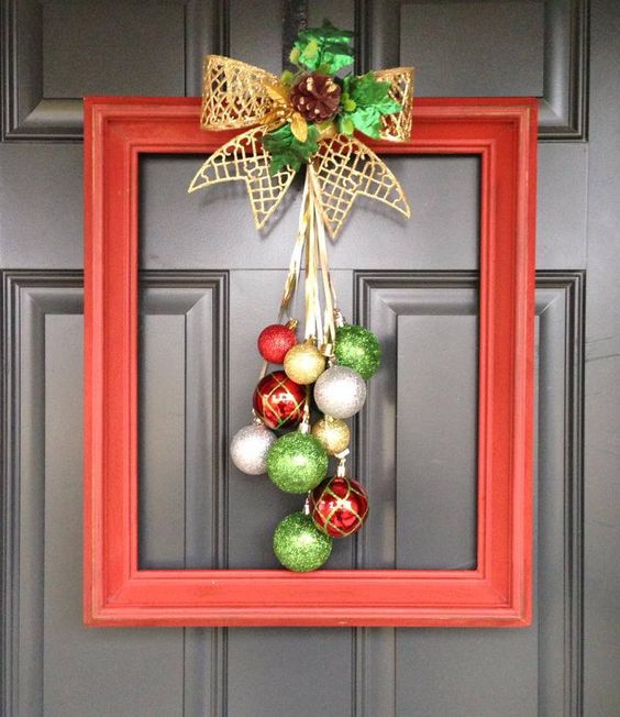 a bright frame Christmas wreath with silver, gold, red and green ornaments, a gold bow with greenery and a pinecone