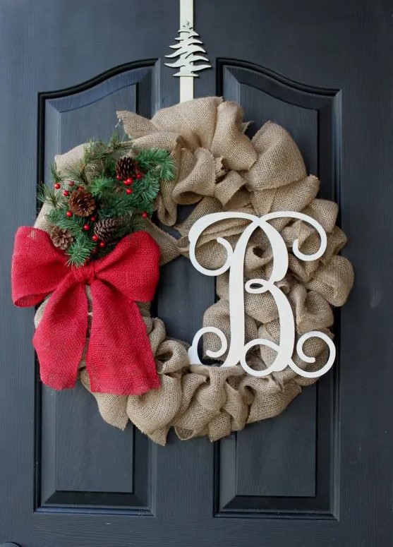 a burlap wreath with a monogram, a red bow and evergreens and pinecones for a chic look