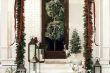 a charming Christmas porch with an evergreen and red ribbon garland, wild woodland wreaths, mini trees, candle lanterns and deer figurines