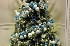 a chic Christmas tree with blue, silver and white ornaments, snowflakes, lights and white branches and deer on top